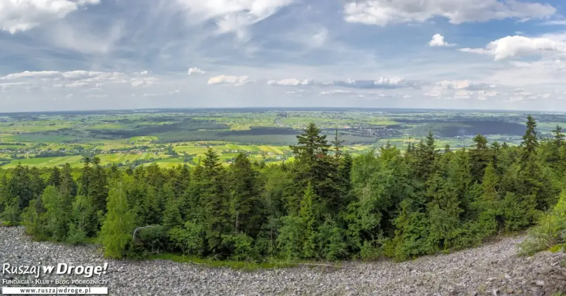 Widok z góry na zielone pola i lasy, idealne na fajne miejsca w świętokrzyskim na weekend. Kamieniste zbocze i chmury na niebie.