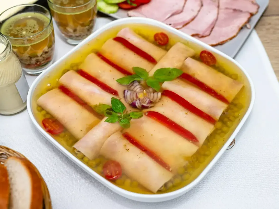 Szynka w galarecie z groszkiem, papryką i pomidorkami. Obok majonez, pieczywo i plastry wędliny.