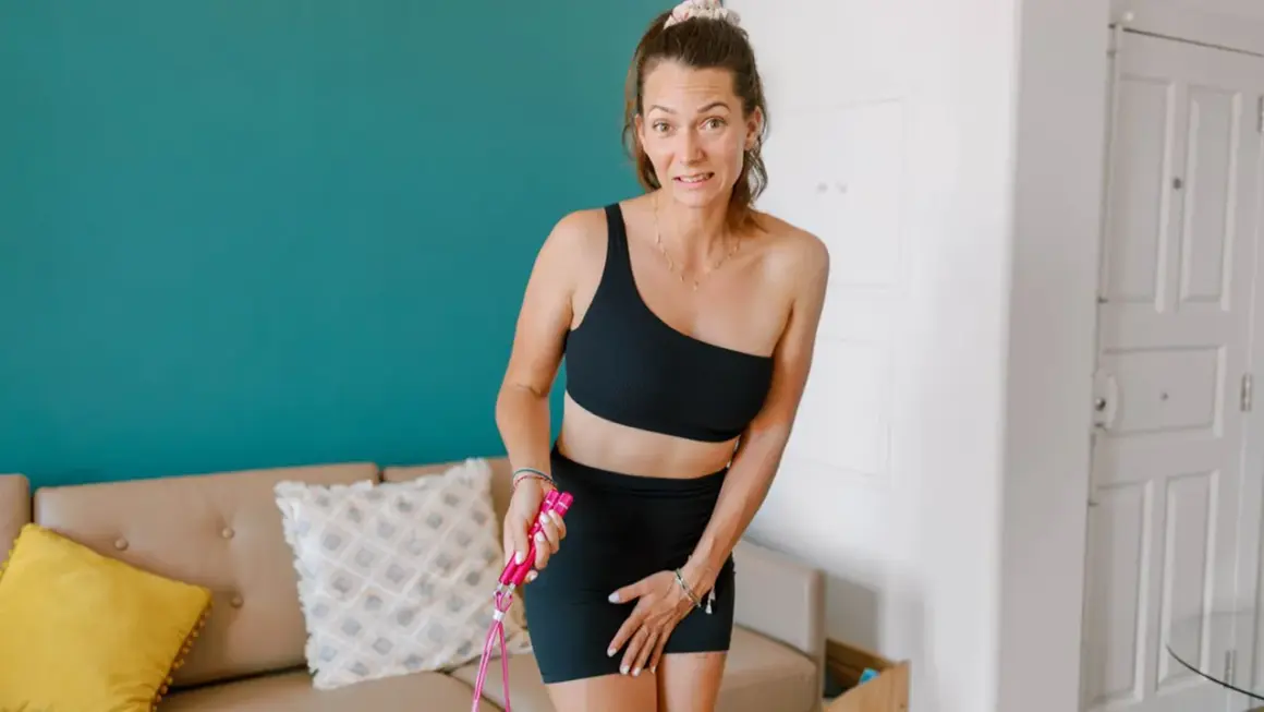 Femme en tenue de sport, tenant une corde à sauter, semble gênée par une fuite urinaire après le sport.