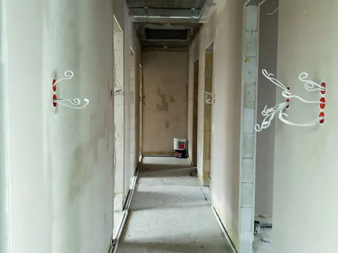 Korytarz w budowie. Widać przygotowane otwory pod puszki elektryczne z wystającymi przewodami. To ważny etap, co zrobić przed tynkami, by uniknąć późniejszych przeróbek.