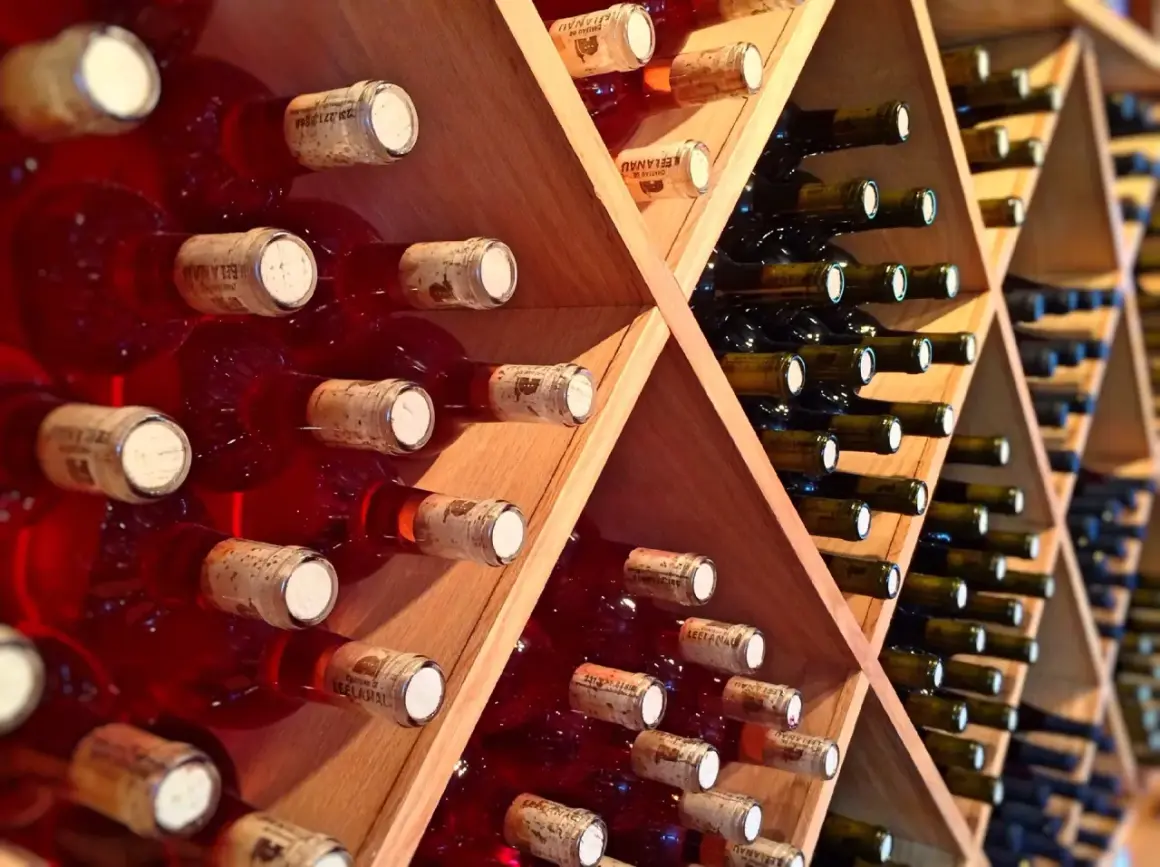 Scaffale in legno con bottiglie di vino rosse e scure, disposte con la corretta inclinazione per la conservazione.