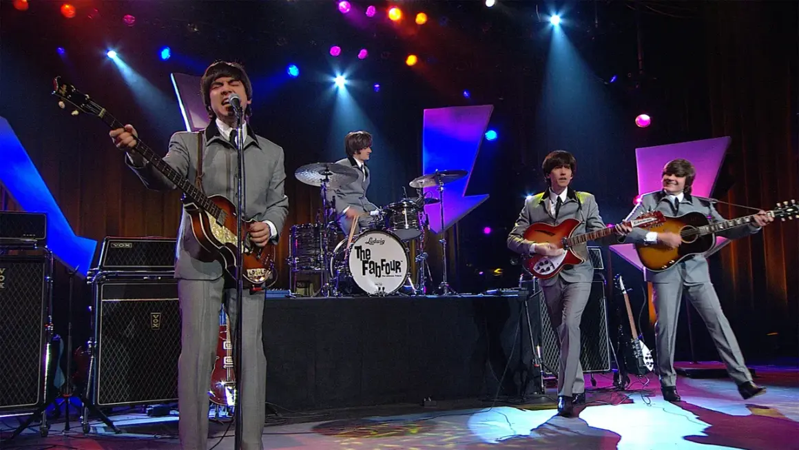 Una cover band sul palco, con abiti grigi e chitarre, ricorda i Fab Four.