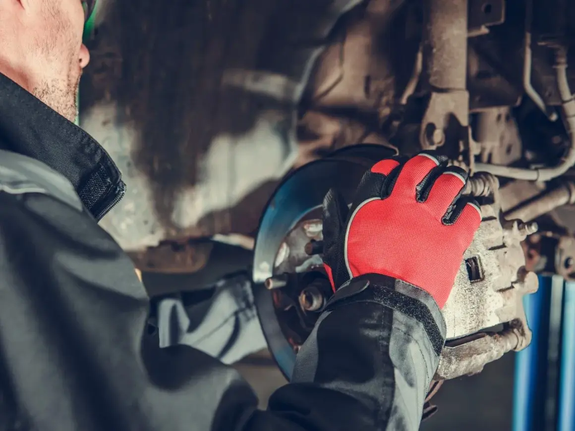 Mechanik w czerwonych rękawicach pracuje przy hamulcach, przygotowując wymianę przewodów hamulcowych.