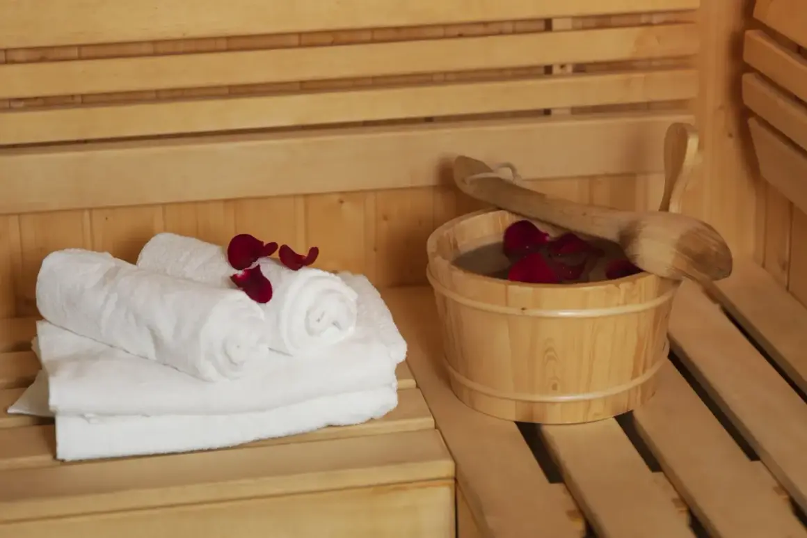 Białe ręczniki i drewniane wiaderko z wodą i płatkami róż w saunie. Dylemat: najpierw sauna sucha czy parowa?