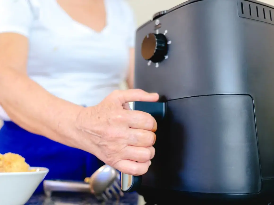 Dłoń osoby wyciąga szufladę frytkownicy beztłuszczowej, pokazując, jak działa air fryer.