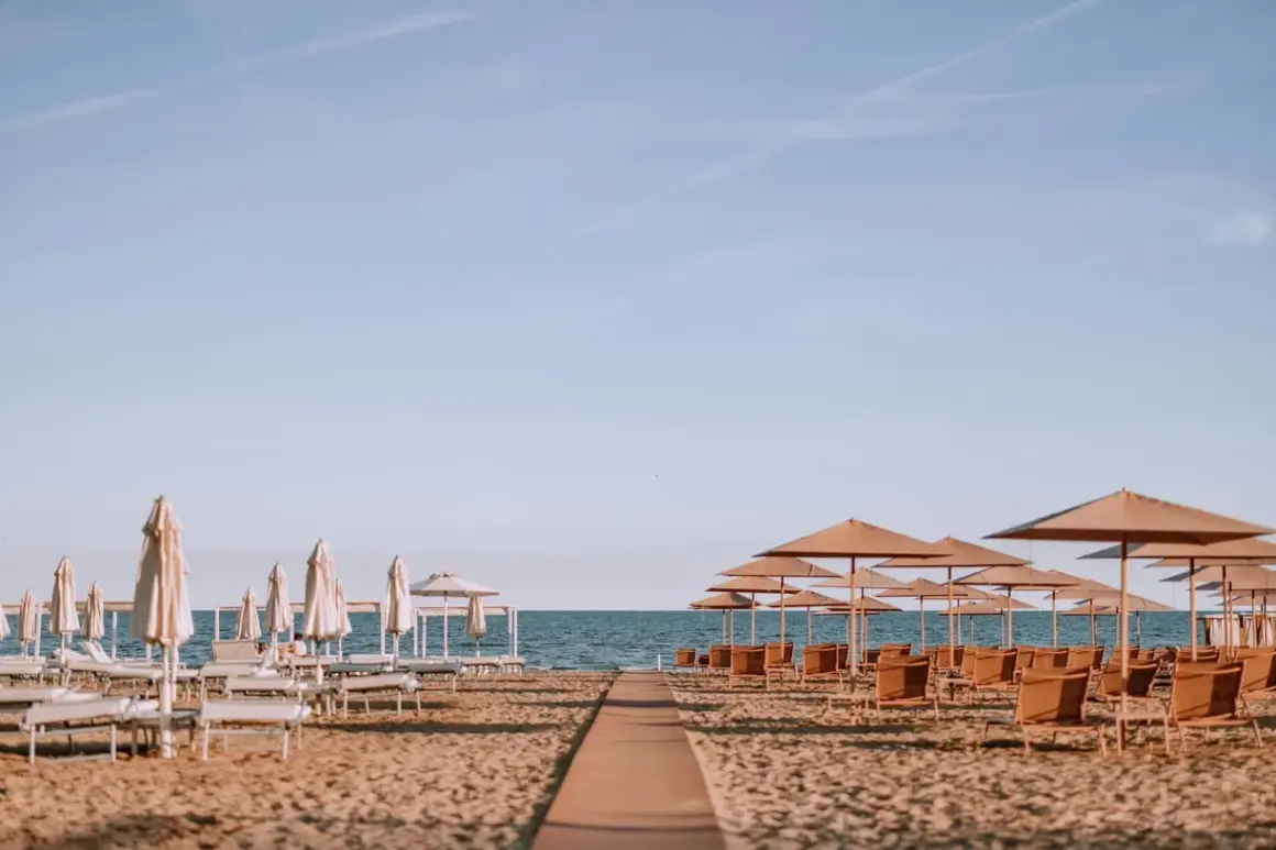 Ombrelloni e lettini pronti per accogliere i bagnanti sulla riviera romagnola, con il mare calmo all'orizzonte.