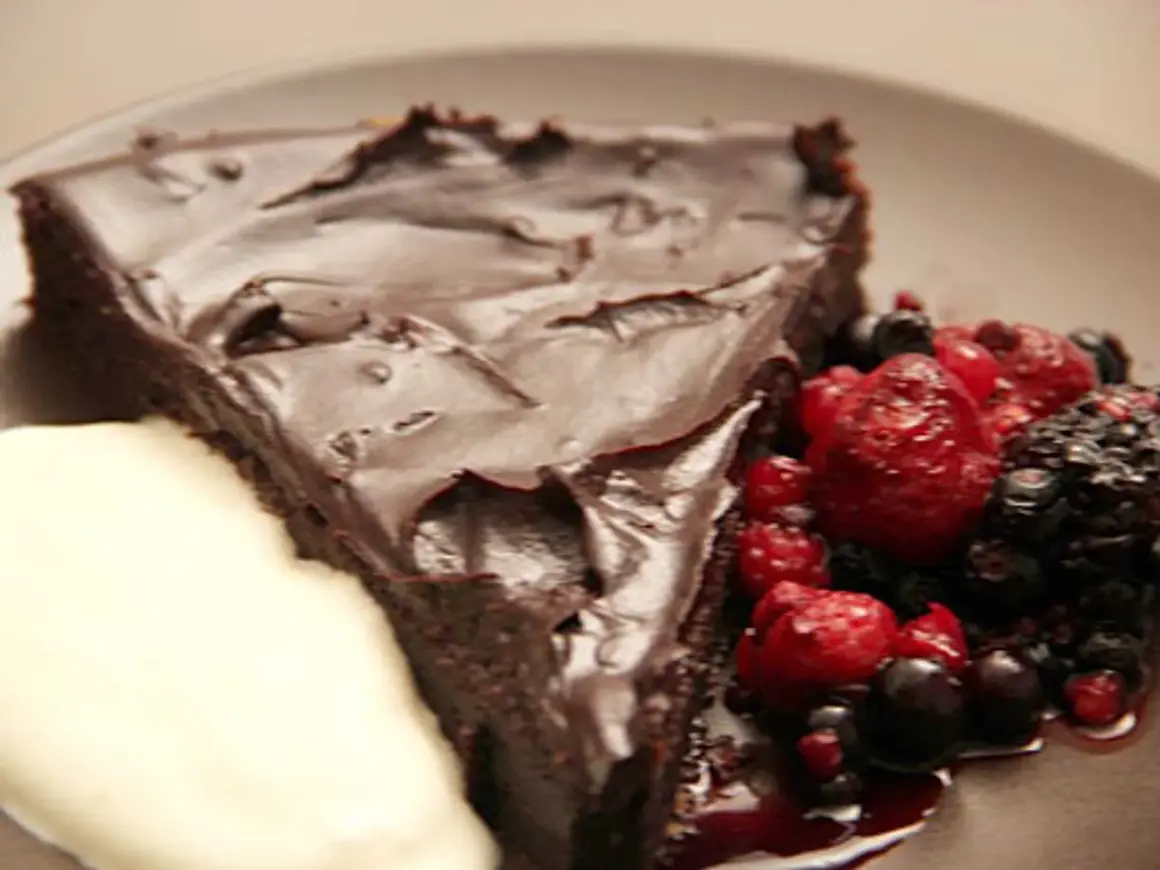 En bit chokladkaka med tryffel, toppad med mörk chokladglasyr, serveras med färska bär och en klick grädde.
