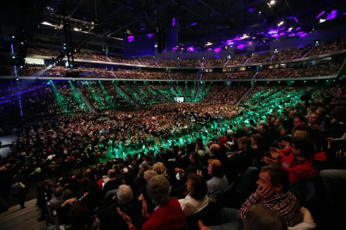 Tausende Menschen in einer Arena, beleuchtet von grünen und violetten Lichtern. Eine beeindruckende Kulisse für eine mega church Veranstaltung.