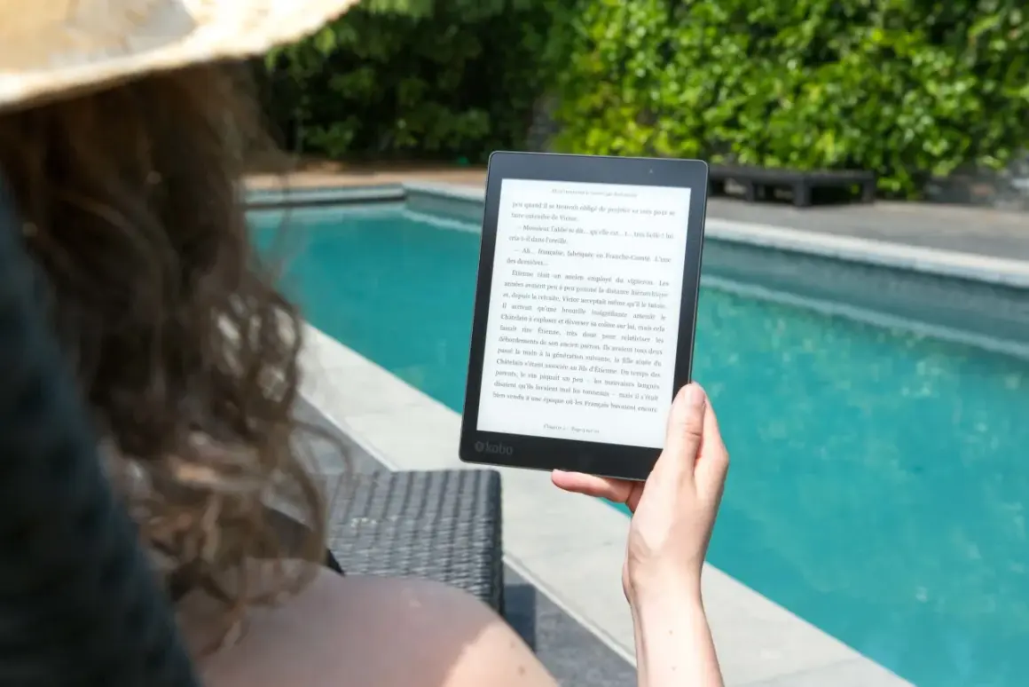 Une personne lit un epub en ligne au bord d'une piscine, profitant du soleil et d'une lecture immersive.