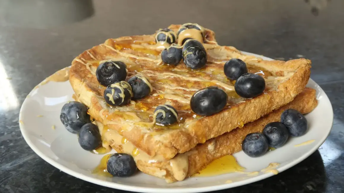 Goldbrauner French Toast Protein-Stapel mit Erdnussbutter, Honig und Blaubeeren.