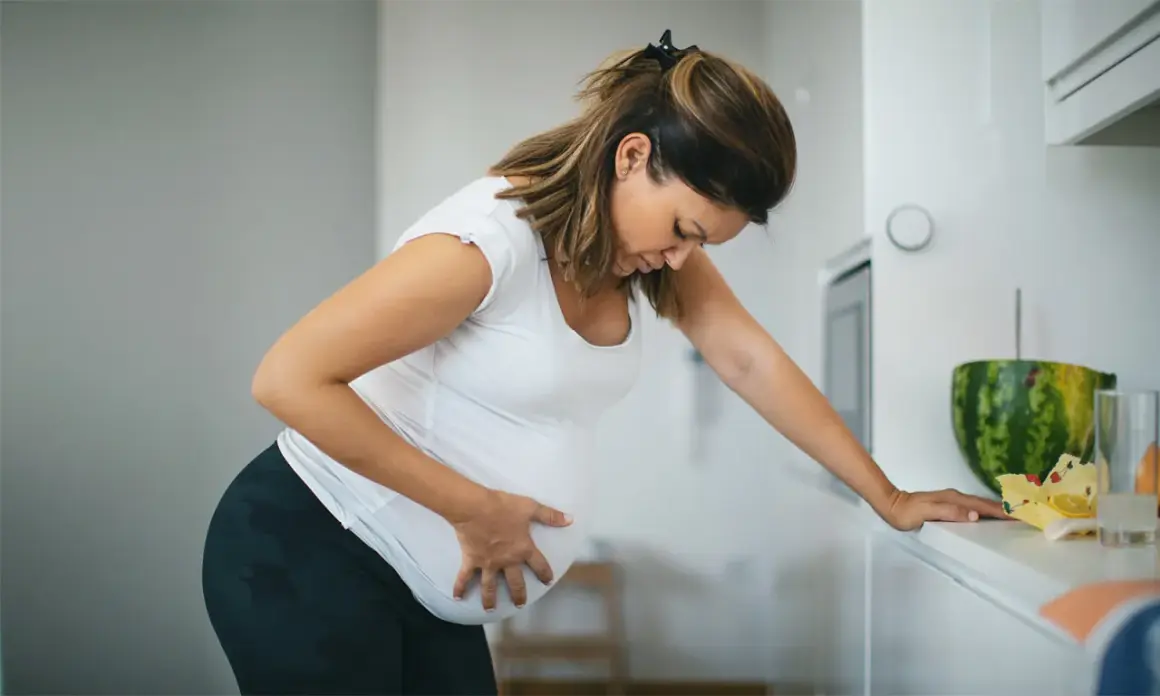 Schwangere Frau mit Hand auf dem Bauch, die sich vorbeugt. Sie fragt sich, ab wann Vorwehen auftreten können.