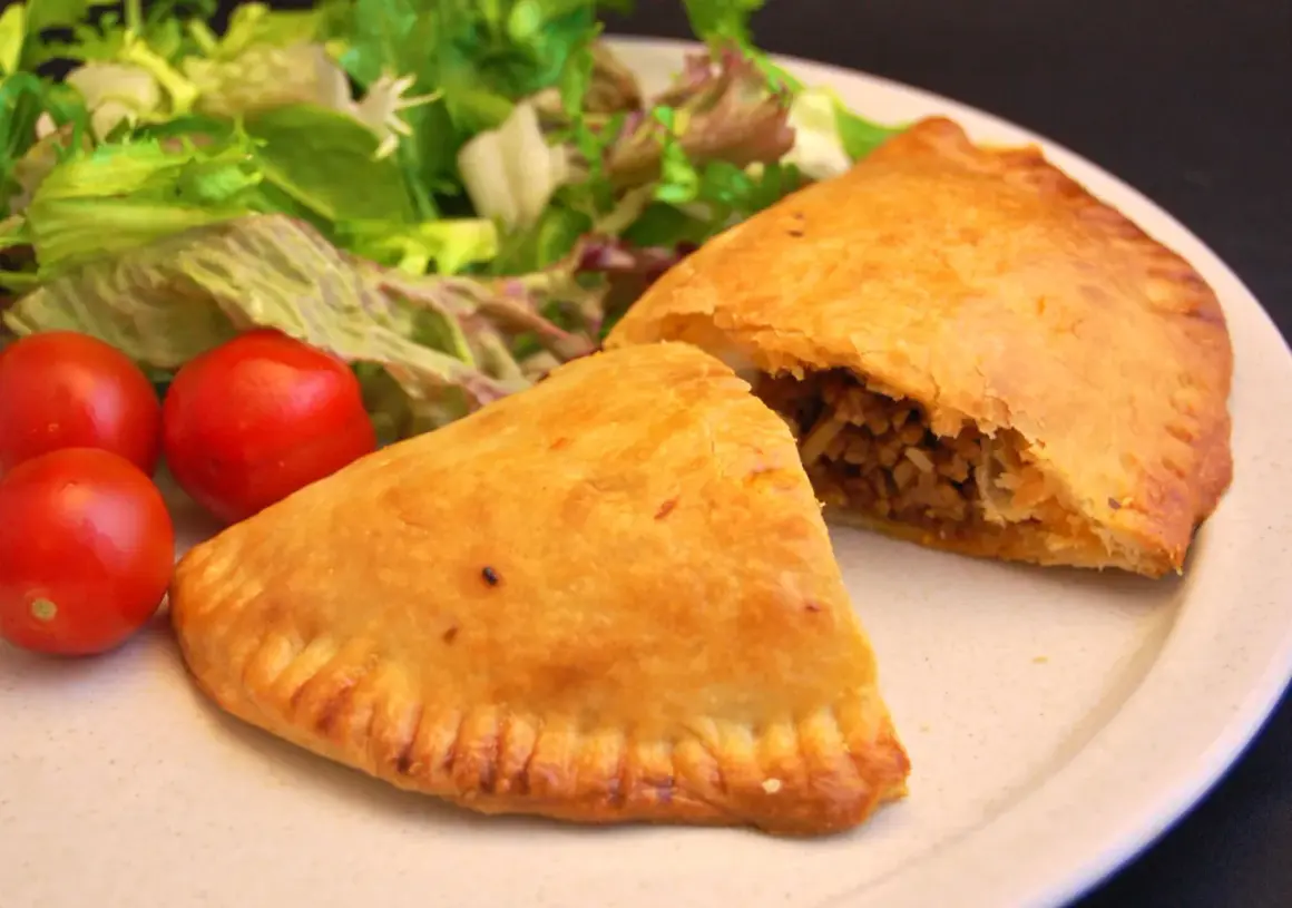 Gyldene empanadas med köttfyllning, serverade med färsk sallad och tomater. Ett perfekt recept för en smakrik måltid.