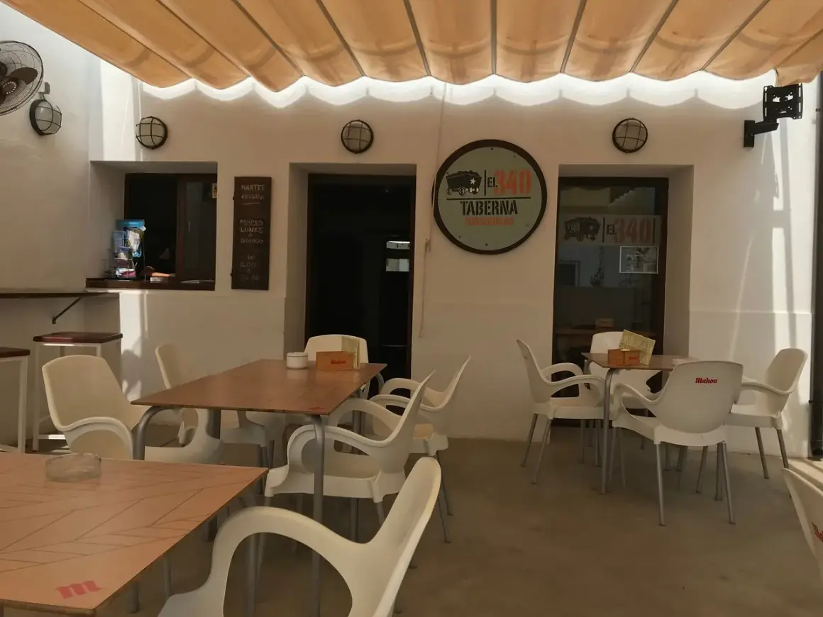 Terraza del restaurante 340, con mesas y sillas de plástico blanco bajo un toldo beige.