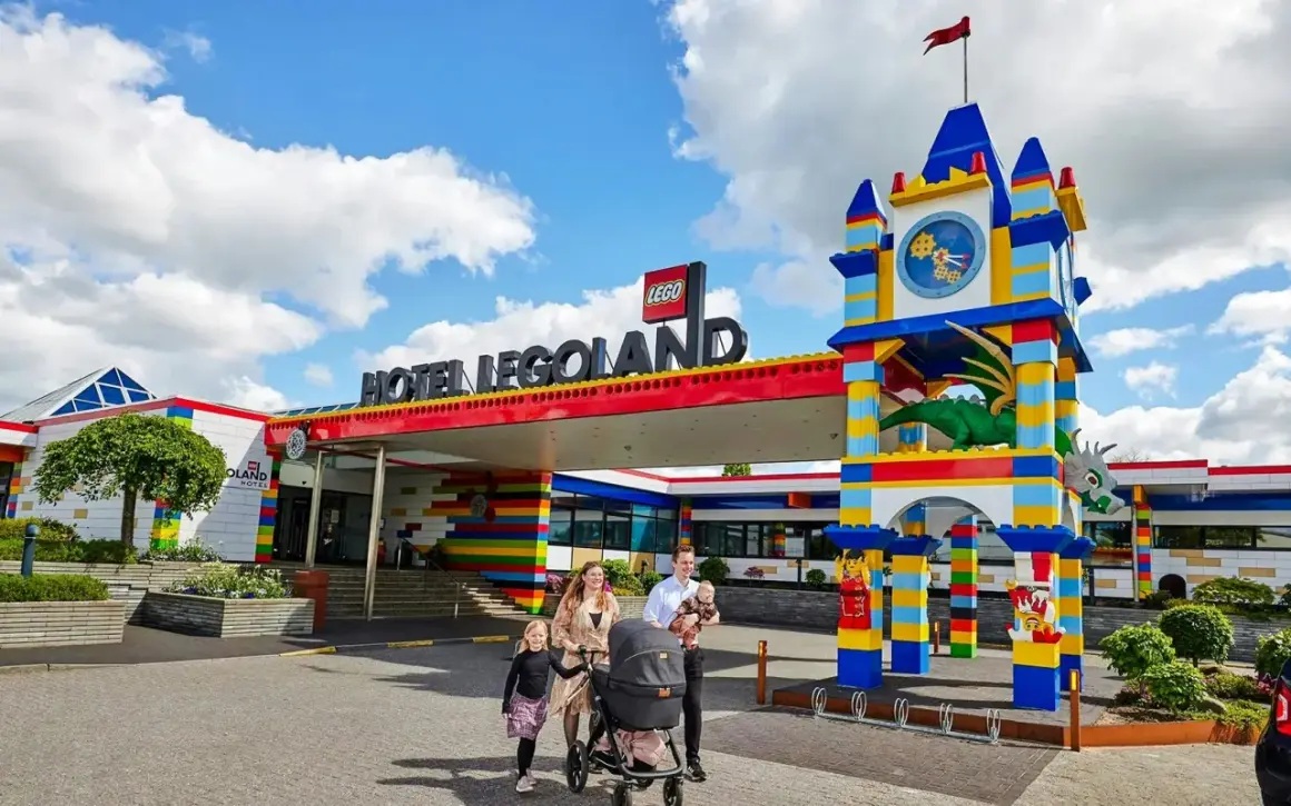 Rodzina z wózkiem spacerowym przed kolorowym hotelem Legoland Kopenhaga. Smoczy zegar i wejście z klocków LEGO.