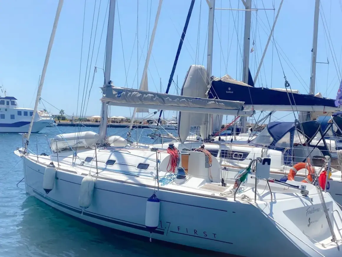 Barca a vela bianca ormeggiata, con scritte "17 FIRST" e "Finistère". Dettagli tecnici e mare calmo.