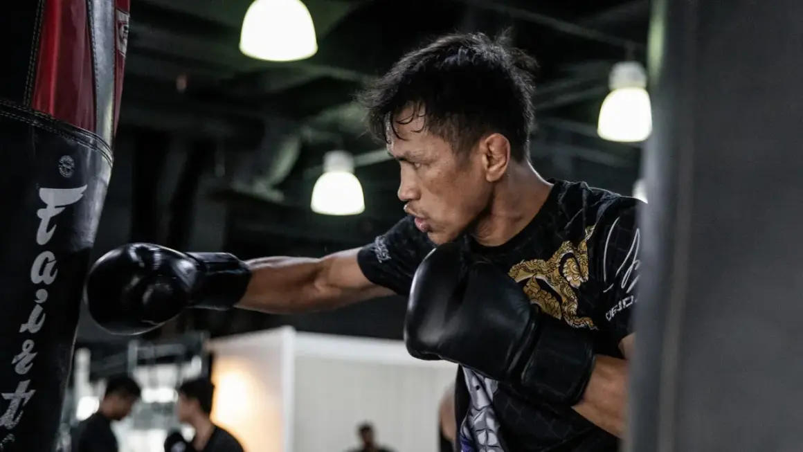 A boxer practices his form, throwing a punch at a heavy bag. His focus is intense as he trains.