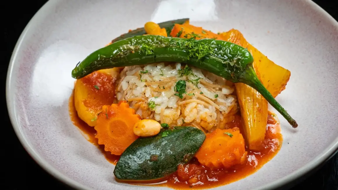 Herzhaftes Reisgericht mit viel Gemüse, darunter Karotten, Zucchini und eine grüne Chilischote, serviert in einer roten Sauce.