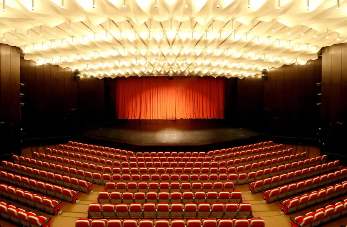 Leere rote Sitze im **Theater und Konzerthaus Solingen** warten auf Besucher. Die Bühne ist mit einem roten Vorhang verdeckt.