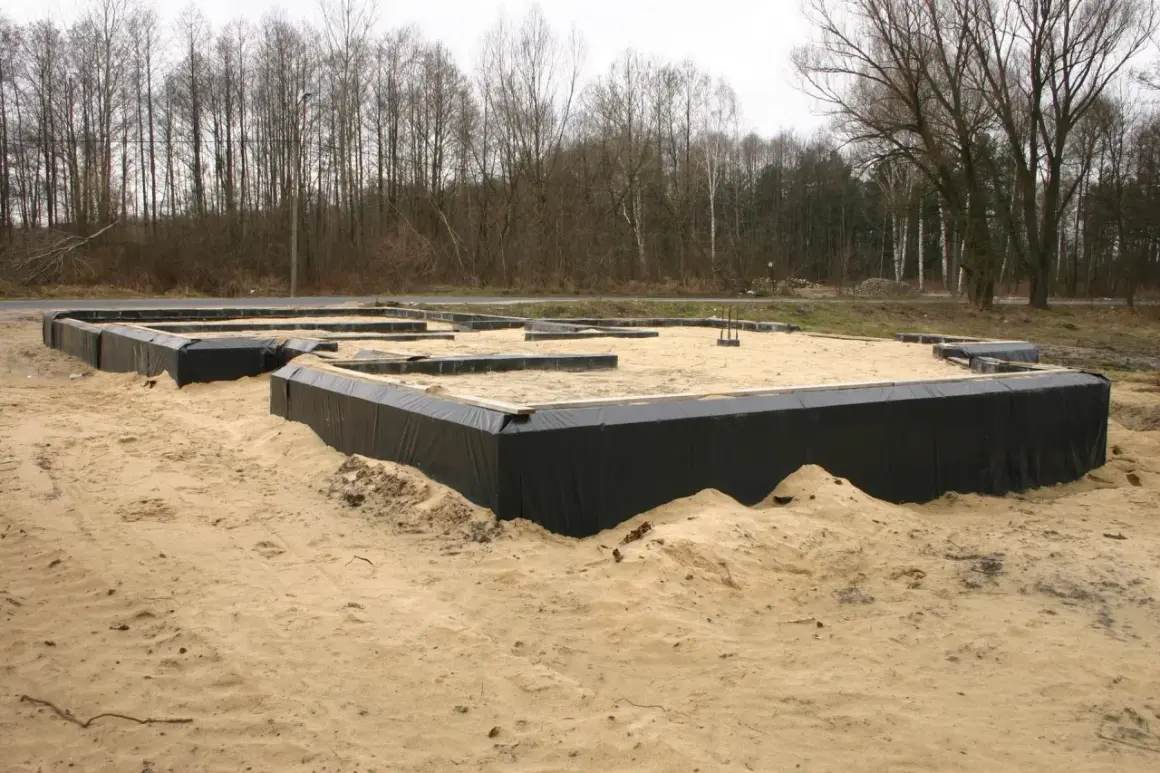Fundamenty domu w piasku, otoczone czarną folią. W tle las. Wkrótce powstanie tu chudy beton.