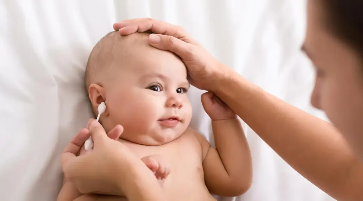 Delikatne czyszczenie uszu niemowlaka. Mama ostrożnie używa patyczka higienicznego, by zadbać o higienę maluszka.