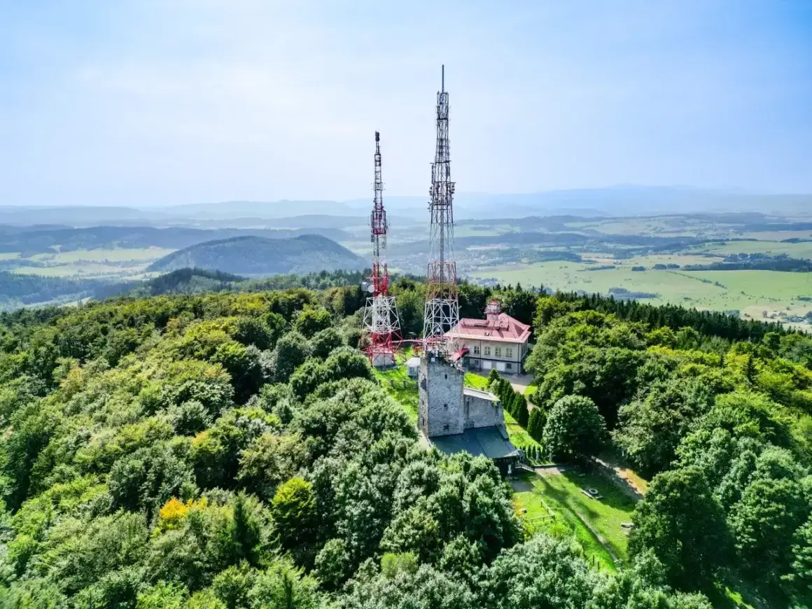 Wieże telekomunikacyjne na zalesionym szczycie Chełmiec. W tle rozległa panorama krajobrazu.