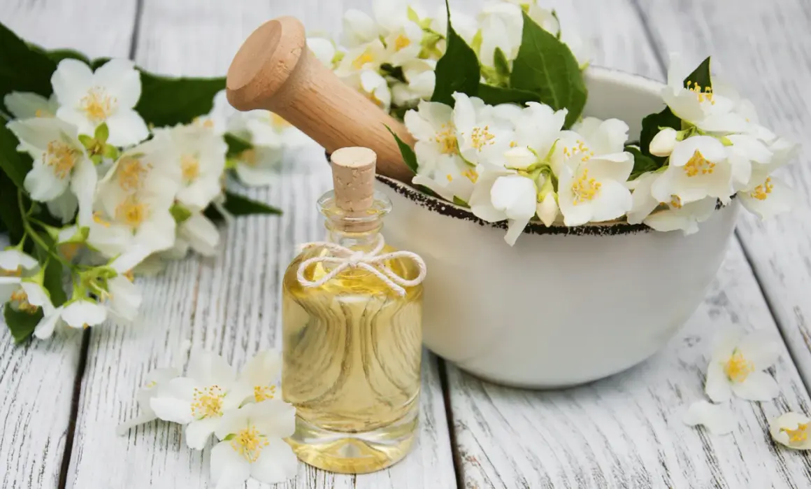 Jasminöl in einer Flasche, umgeben von Blüten. Die Jasmin Wirkung auf die Psyche ist beruhigend und stimmungsaufhellend.