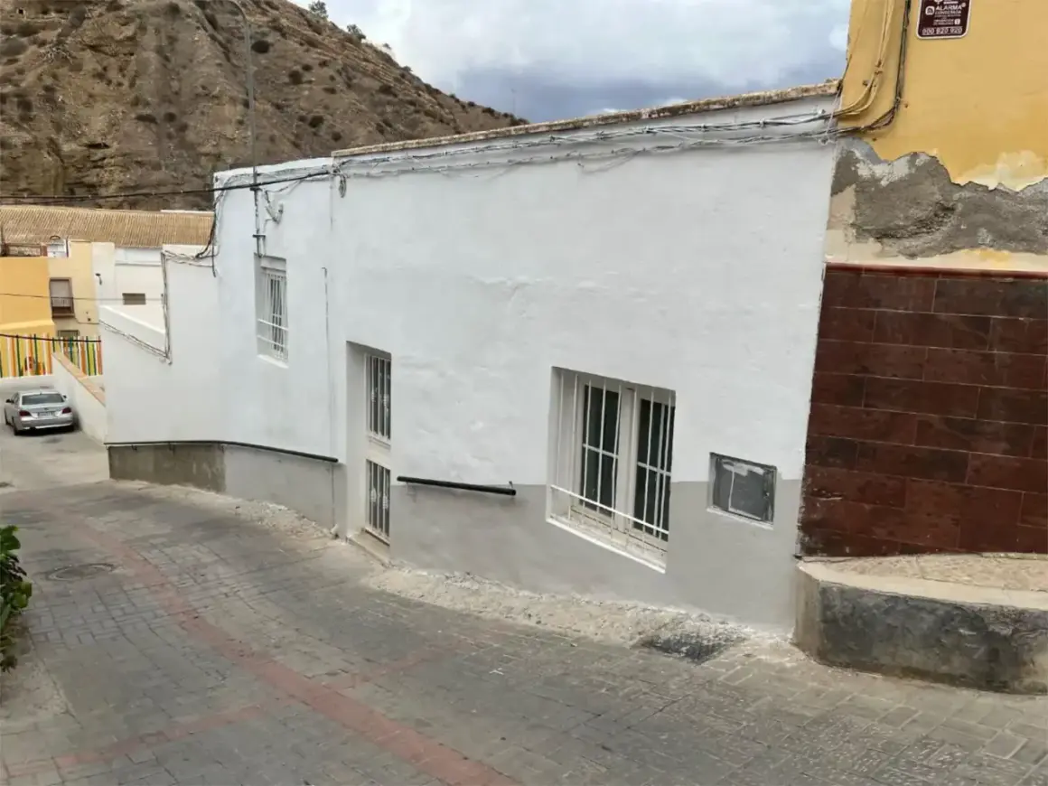 Calle empedrada en un pueblo blanco de Andalucía, con casas encaladas y una ladera rocosa al fondo. Un coche plateado aparcado. Gador, Almería.