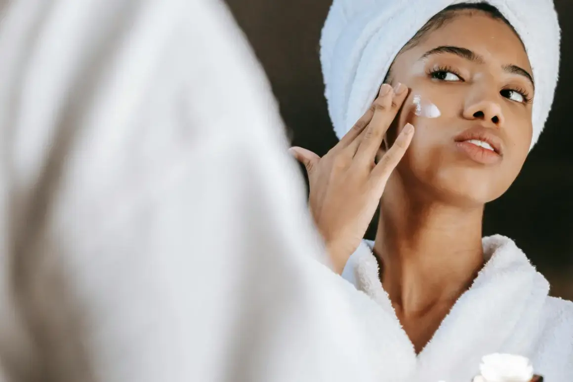 Frau mit Handtuch auf dem Kopf trägt Creme auf, die Glykolsäure und Niacinamid enthält.