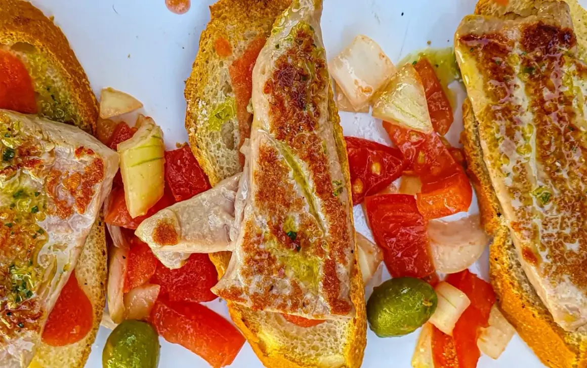Delicioso tapeo en el ejido: tostadas con pescado a la plancha, pimientos, tomate y aceitunas.