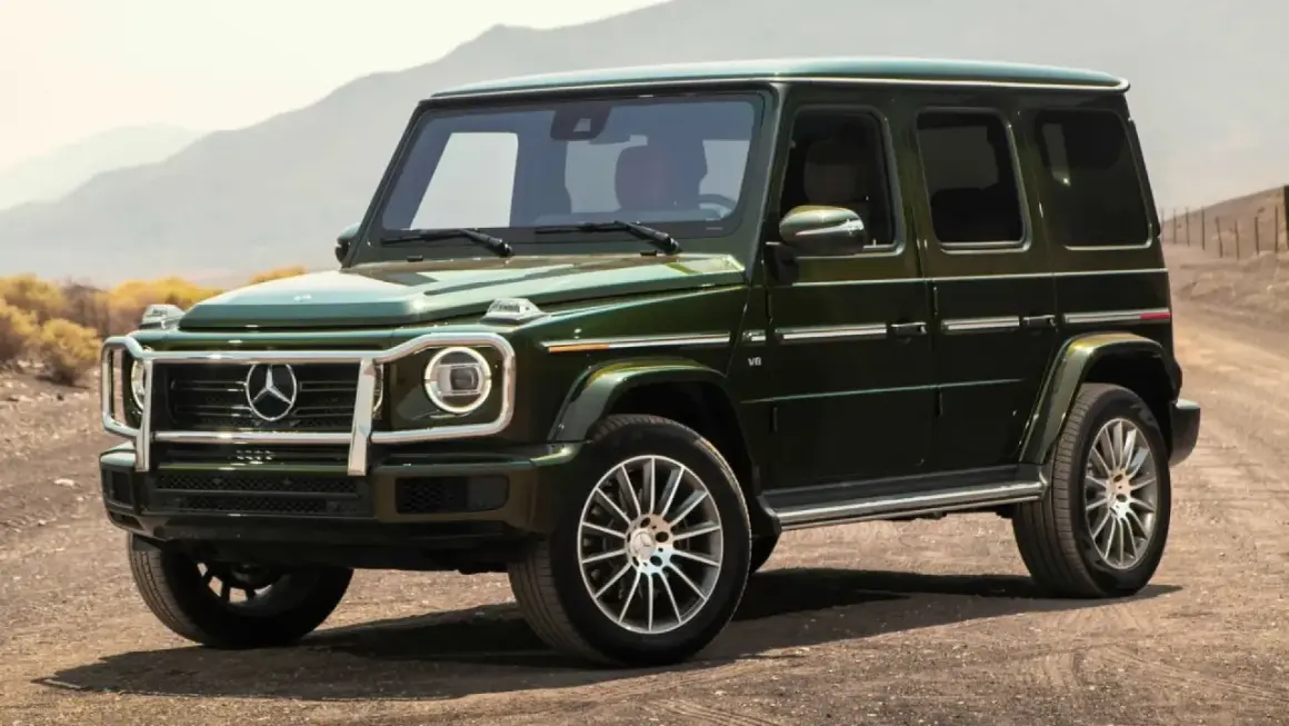 Un imponente Mercedes-Benz verde oscuro, el mejor Mercedes del mundo, se detiene en un camino polvoriento con montañas al fondo.