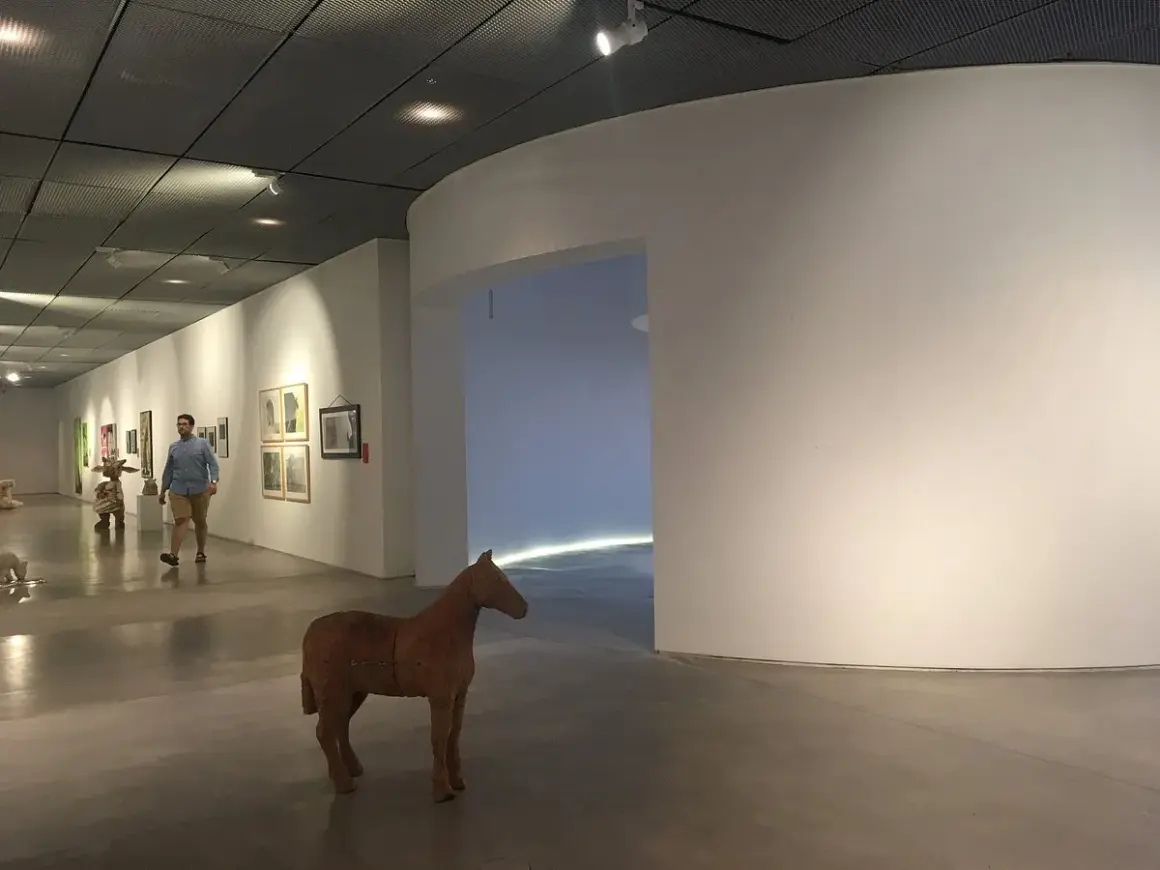 Un hombre pasea por una sala de exposiciones, admirando las obras de arte y una escultura de caballo. Una visita a los museos de Lugo.