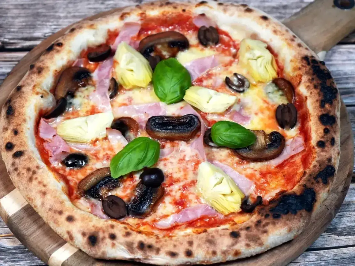 Pizza Capriciosa z klasycznymi składnikami: szynką, pieczarkami, karczochami i oliwkami.