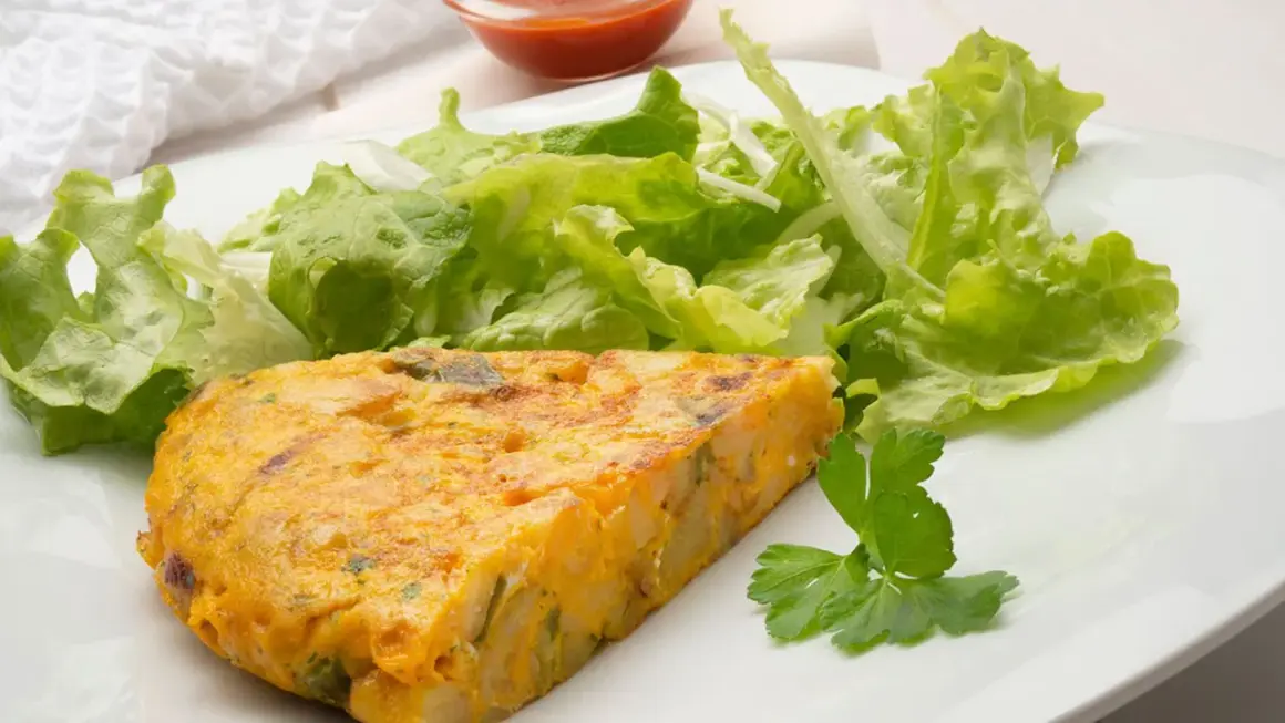 Una porción de tortilla de patatas, dorada y jugosa, acompañada de una fresca ensalada verde y un toque de perejil.