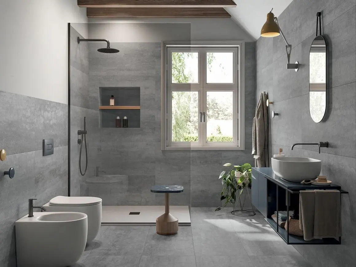 Bagno moderno con piastrelle grigie effetto pietra, doccia walk-in, WC, bidet e lavabo. Ideale per la sostituzione piastrelle bagno.