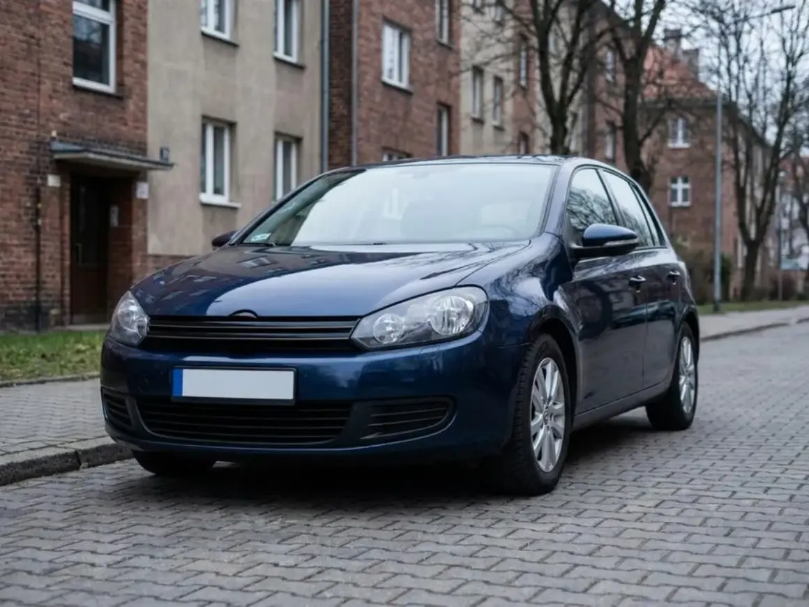 Ciemnoniebieski samochód stoi na brukowanej ulicy przed kamienicą.