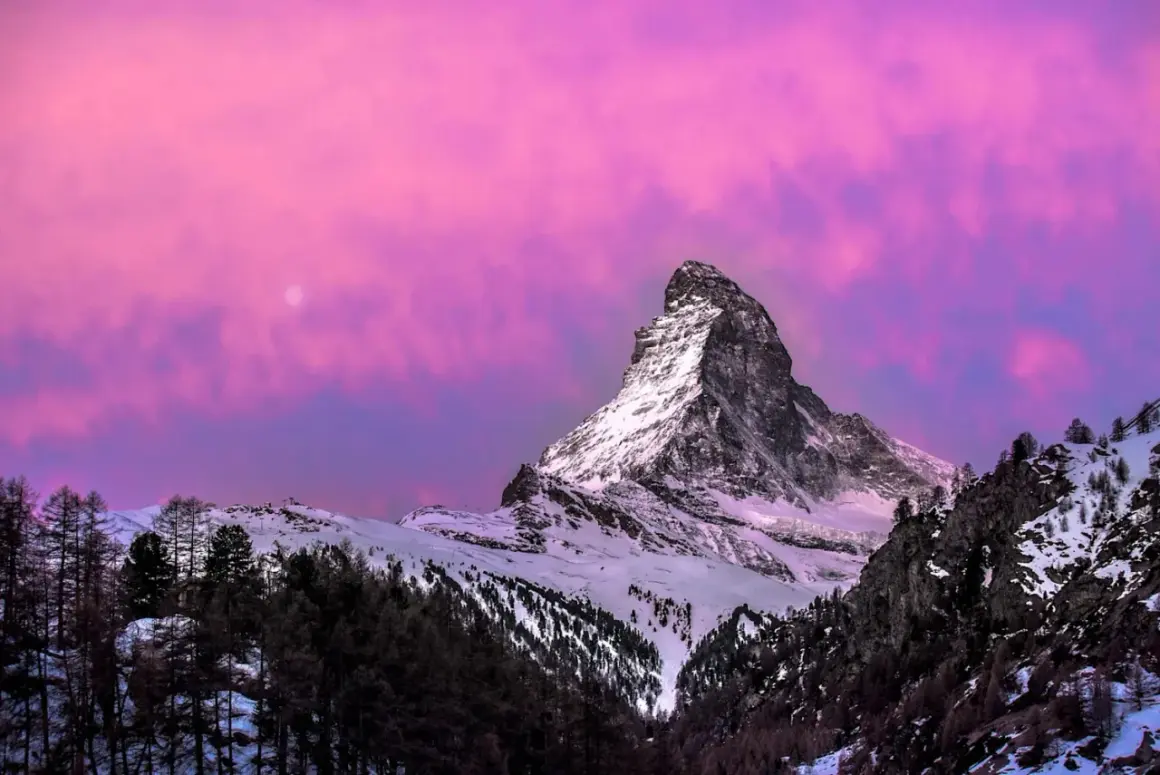 Majestatyczny Matterhorn w różowym niebie, idealny na pierwszy zimowy wypad. Śnieg, lasy i księżyc tworzą magiczny krajobraz.