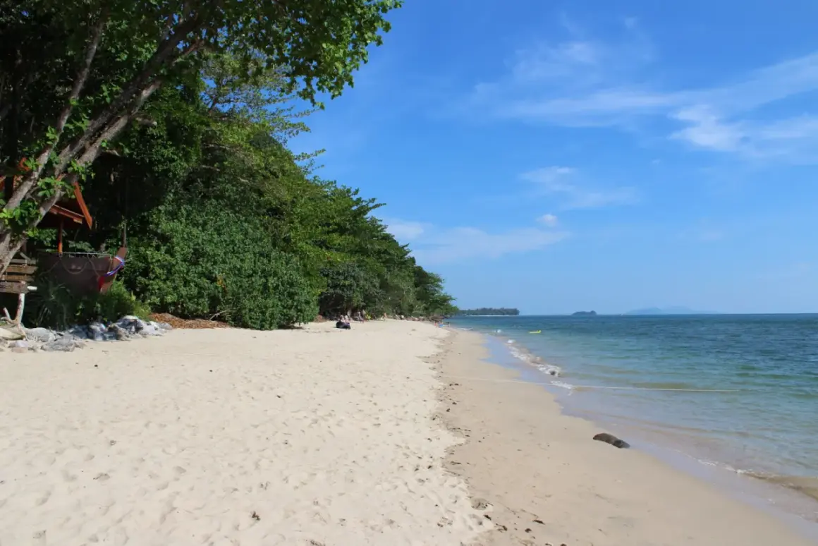 En avkopplande stranddag på Koh Jum. Lång, vit sandstrand kantad av frodig grönska och turkost hav.