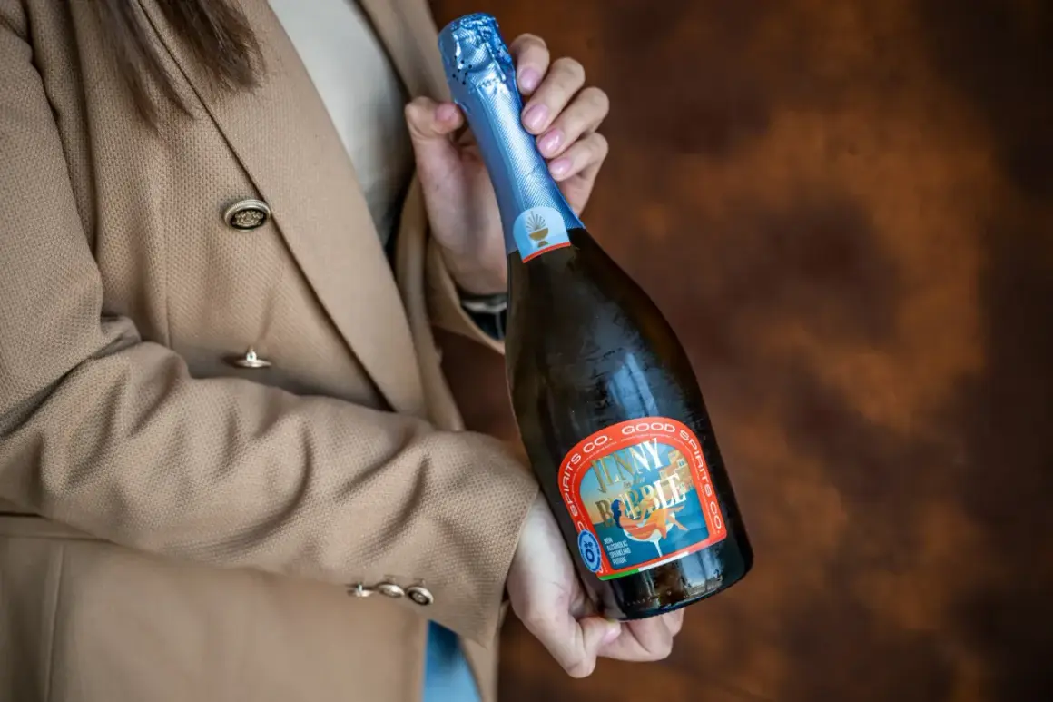 Kobieta w beżowym żakiecie trzyma butelkę musującego napoju, idealnego na międzynarodowy dzień prosecco.