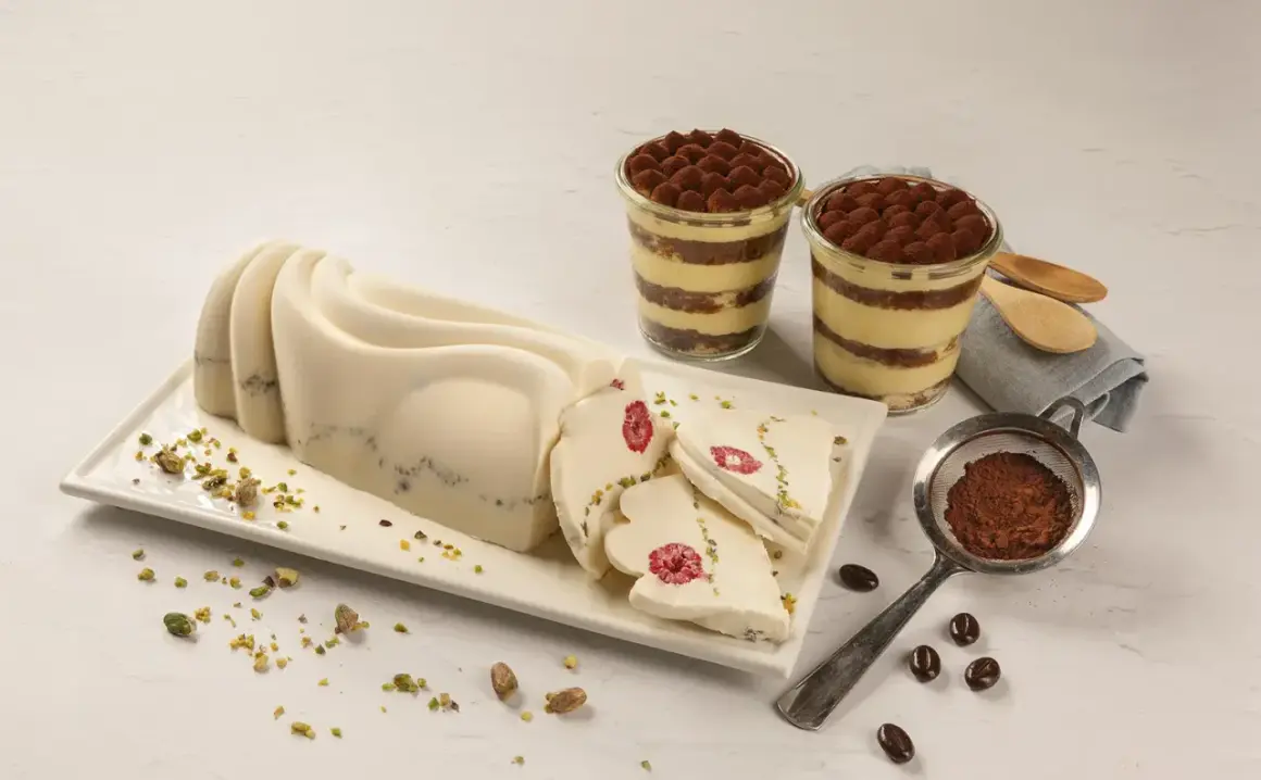Delikatny krem do tortu z mascarpone, udekorowany malinami i pistacjami, obok deserów tiramisu.
