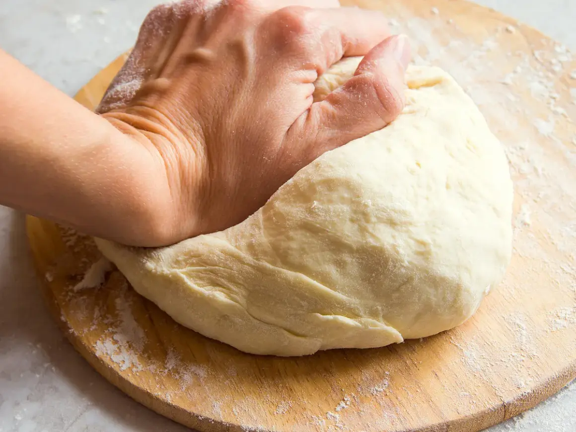 Main d'une personne pétrissant une pâte à pain sur une planche en bois. Une question se pose : pourquoi ma pâte ne lève pas ?