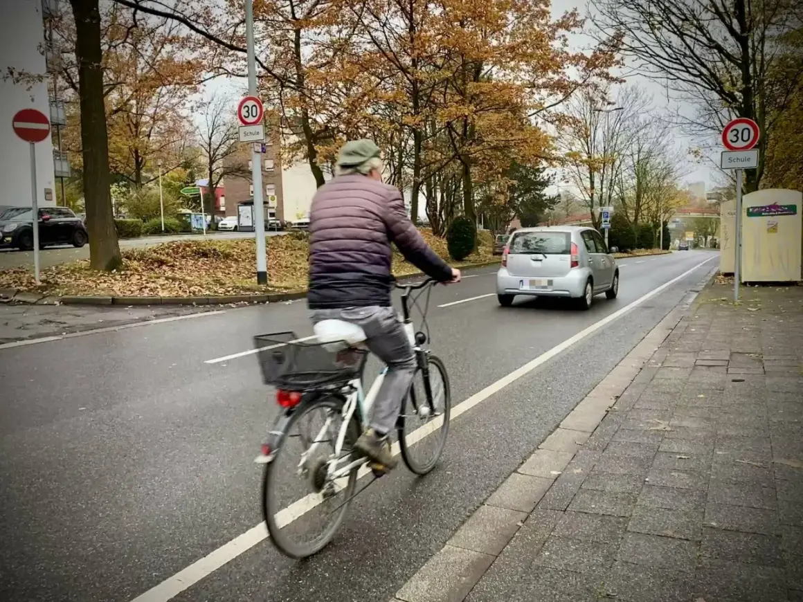 Mann fährt Rad auf einem geschützten Radweg. Ein Auto fährt auf der Straße.