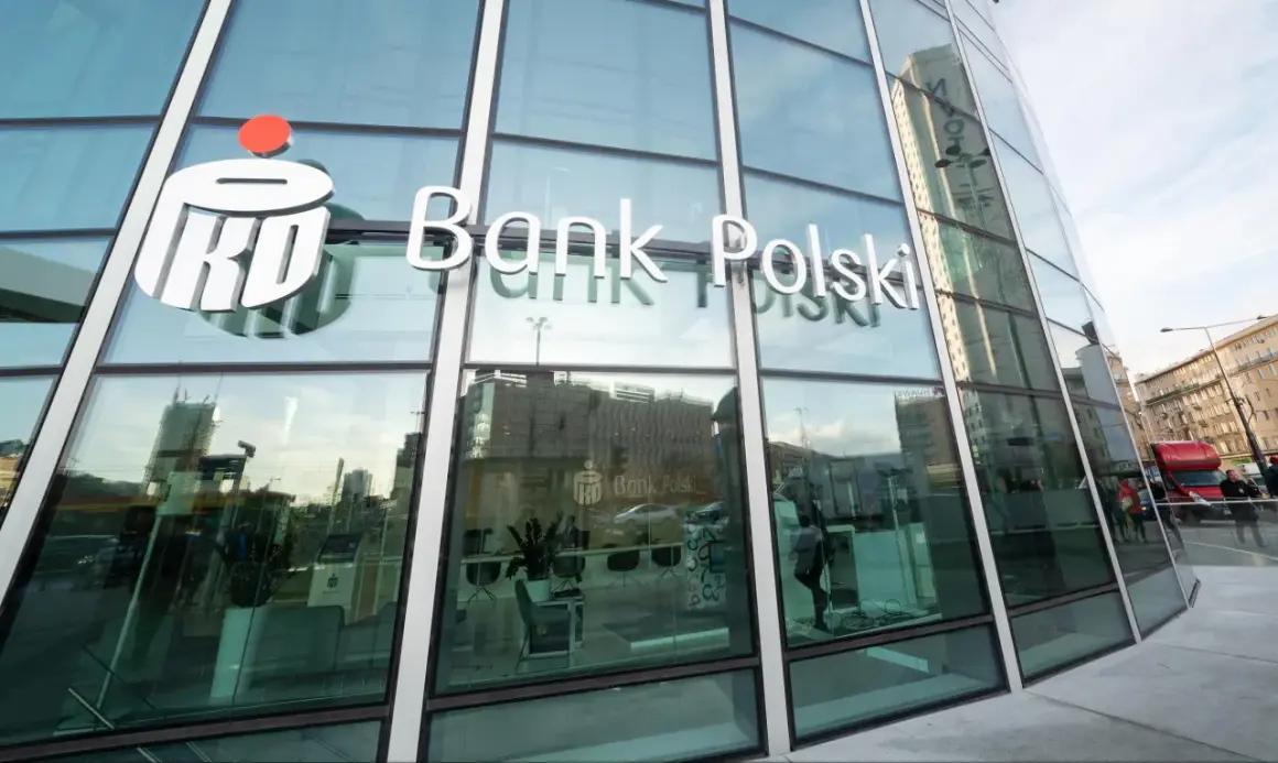 Logo PKO Bank Polski na szklanej fasadzie. W środku wnętrze banku, gdzie można założyć pko bp lokaty.