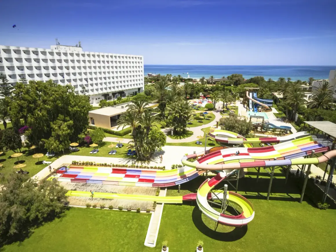 Kolorowy aquapark na plaży w Saharze, z hotelowcem w tle i błękitnym morzem.