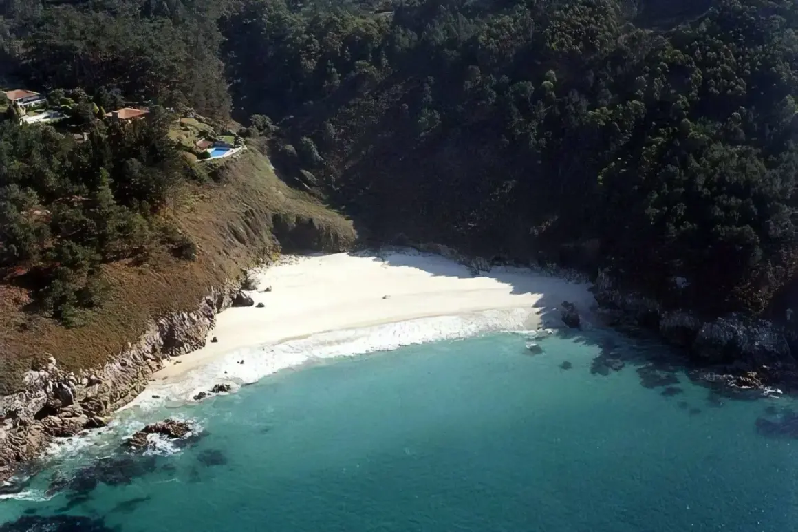 Vista aérea de la playa de San Pedro, Galicia, con aguas turquesas, arena blanca y vegetación exuberante en los acantilados.