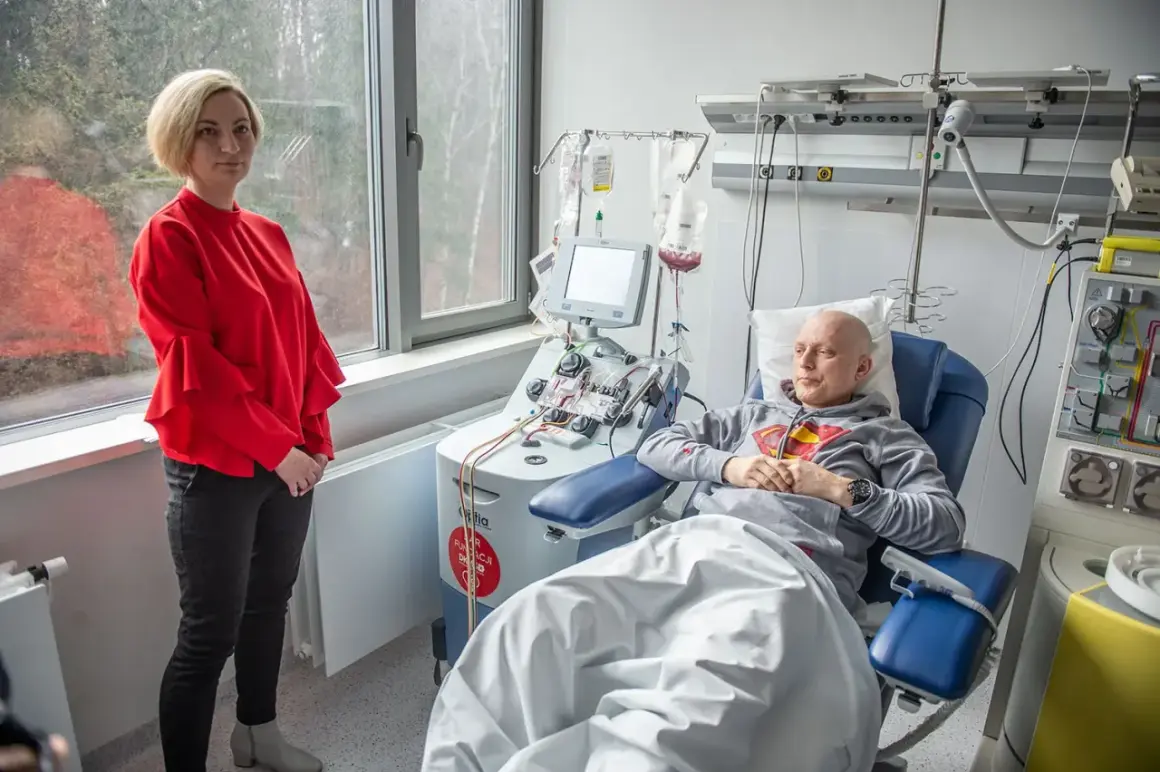 Kobieta w czerwonej bluzce stoi obok pacjenta podłączonego do aparatury medycznej. To ważny moment w procesie przeszczepu szpiku.