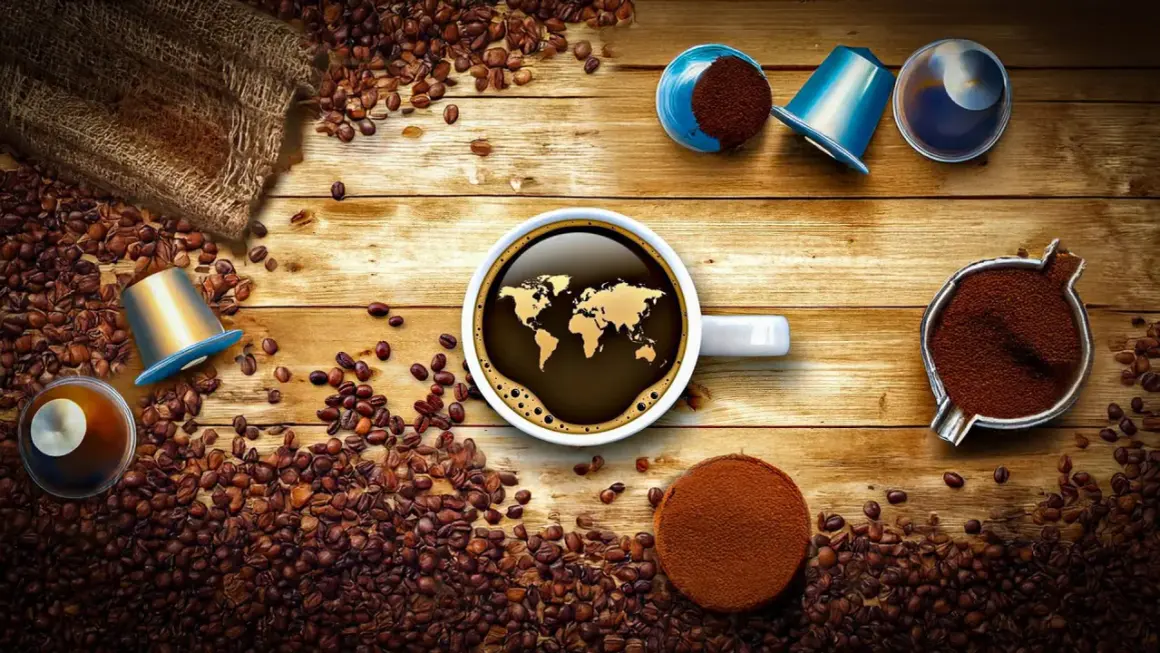Tipi di cialde caffè e chicchi sparsi su un tavolo di legno. Una tazza di caffè con la mappa del mondo riflette il tema globale.