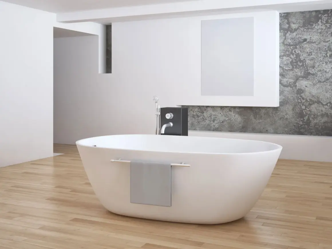 Eine freistehende **Badewanne mitten im Raum** auf hellem Holzboden, daneben ein moderner Wasserhahn und eine graue Handtuchhalterung.