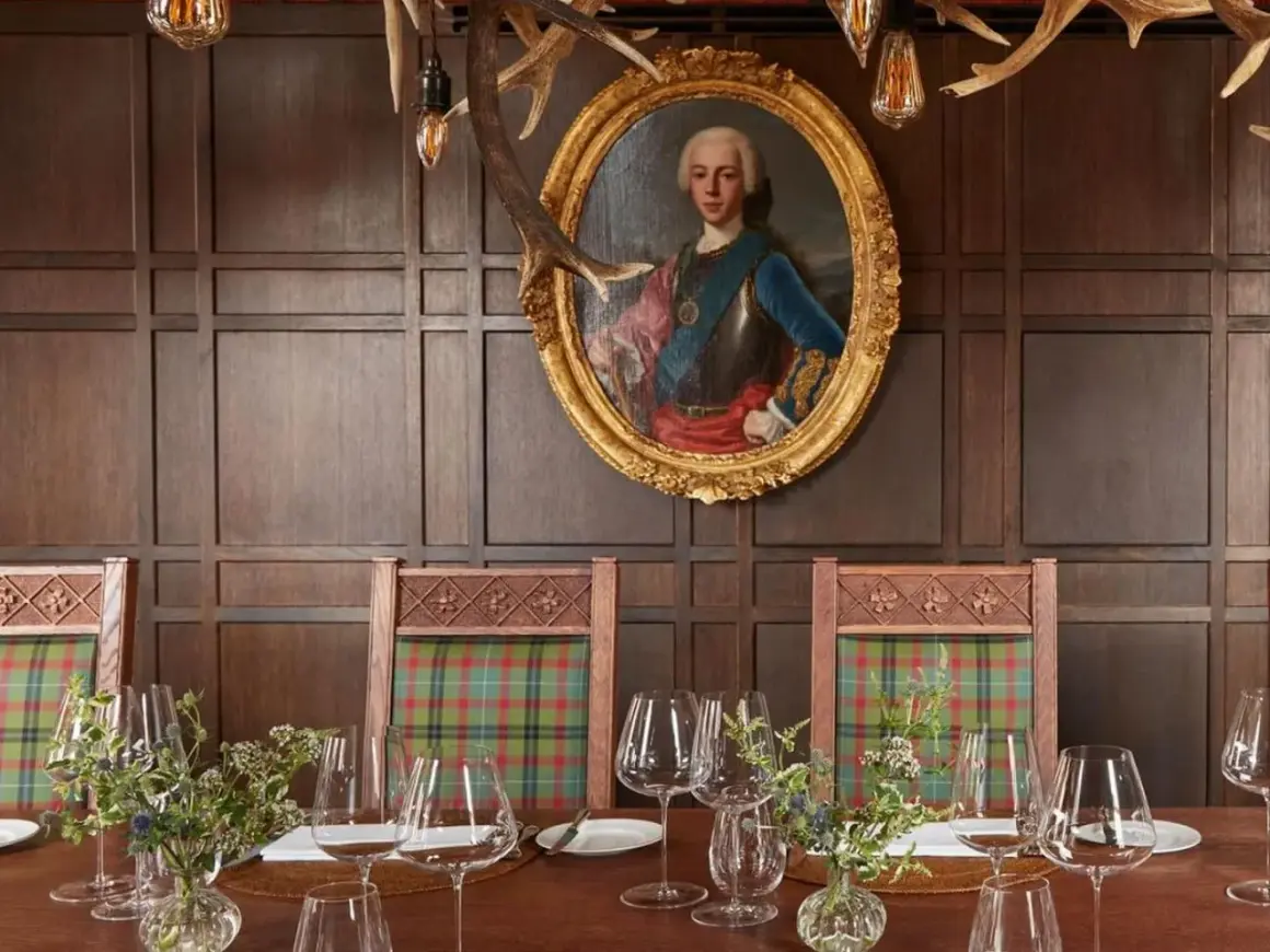 Un ritratto regale domina la sala da pranzo, con sedie a quadri e un tavolo apparecchiato, un'ambientazione che evoca i migliori ristoranti di Londra.