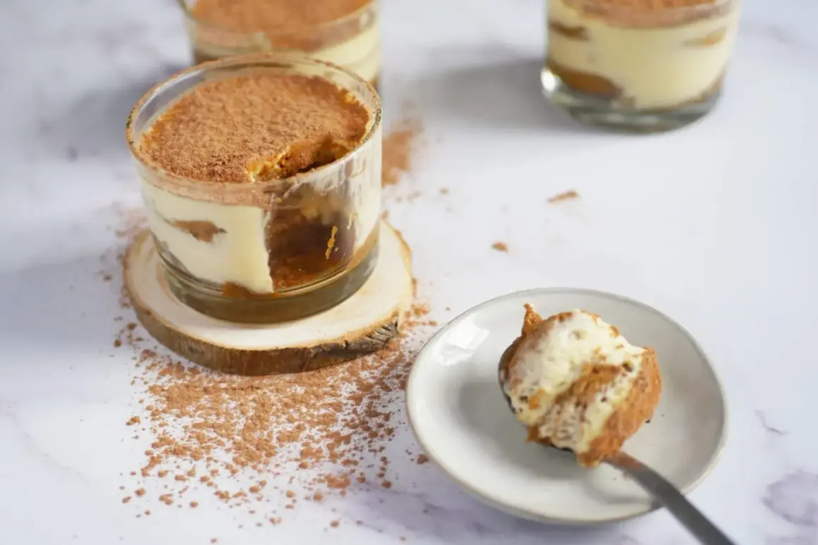 Tiramisu en verrine saupoudré de cacao, avec une cuillère garnie.