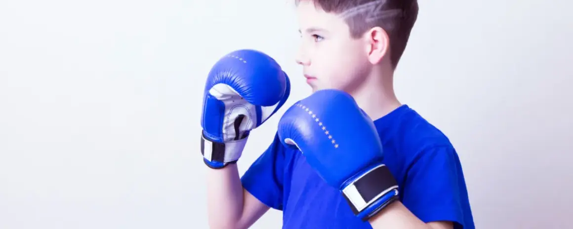 Young boxer in a wide boxing stance, wearing blue gloves and shirt, ready to fight.